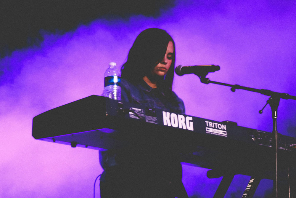 Young woman playing korg keyboard live on a smokey stage