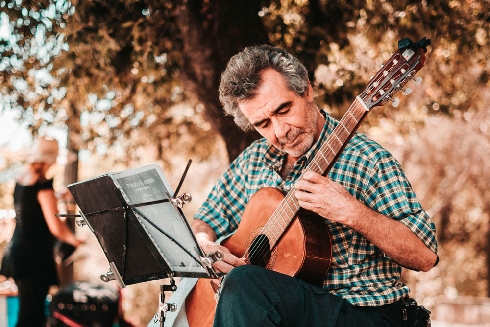 Old man playing classical acoustic guitar in the park